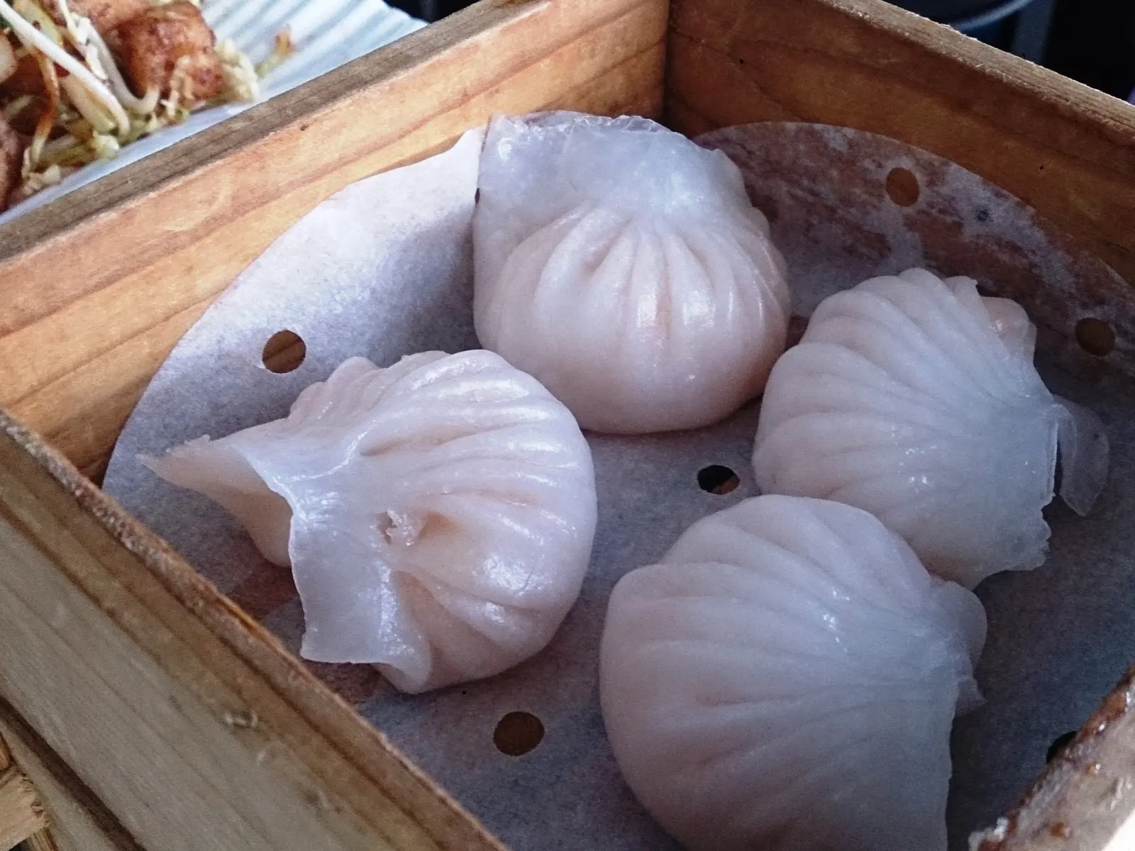 Cuatro har gow translúcidos en una vaporera de madera