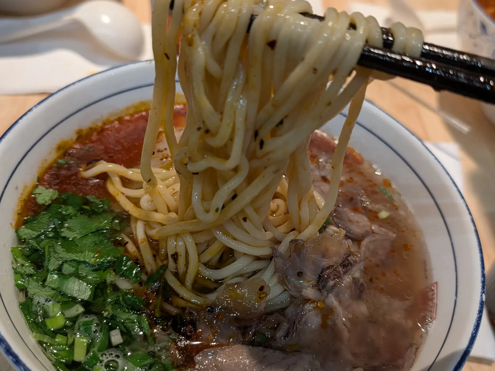 Unos palillos levantan tallarines de un cuenco de sopa con ternera y cebolleta