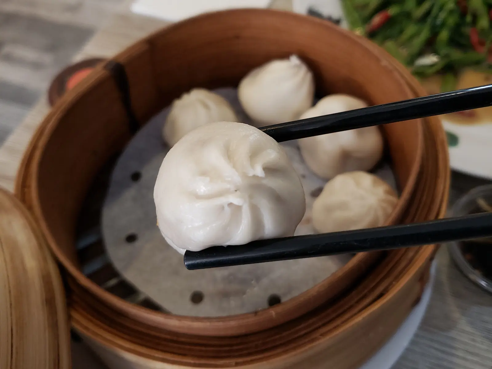 Unos palillos levantan un xiaolongbao de una vaporera de bambú, con los pliegues cerrados en espiral